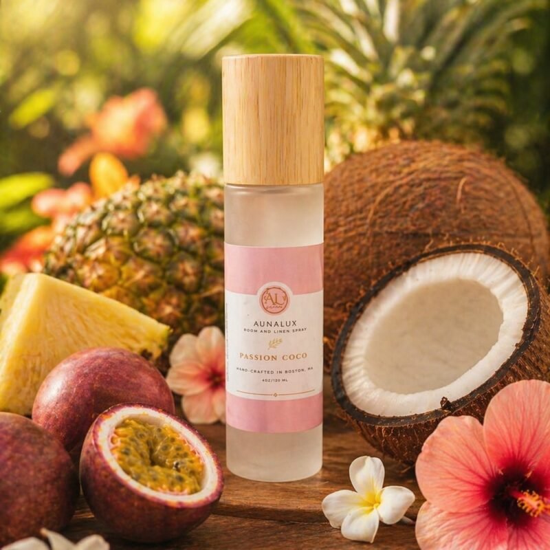 “Aunalux Passion Coco room and linen spray bottle with bamboo lid surrounded by coconut, pineapple, passion fruit, and tropical flowers in a bright tropical setting”
