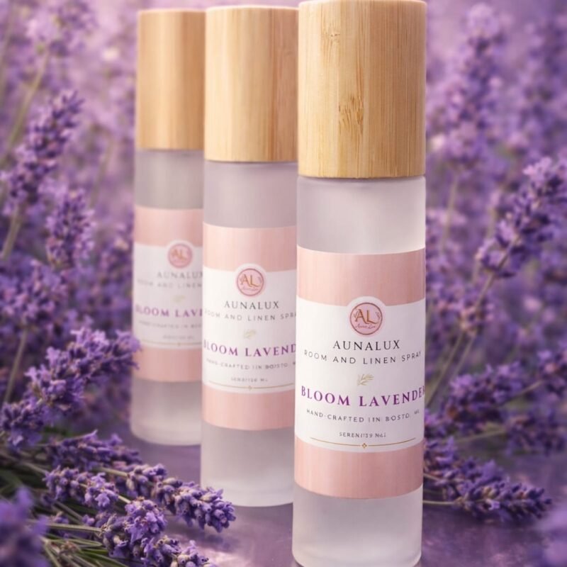 Three Aunalux Bloom Lavender room and linen spray bottles with bamboo lids displayed on a wooden surface with fresh lavender flowers
